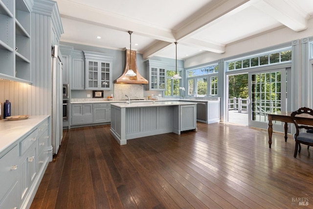 kitchen with premium range hood, hanging light fixtures, a kitchen island with sink, dark wood-type flooring, and beam ceiling