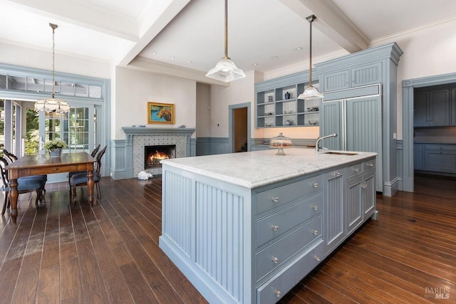 kitchen featuring pendant lighting, beam ceiling, an island with sink, and dark wood-type flooring