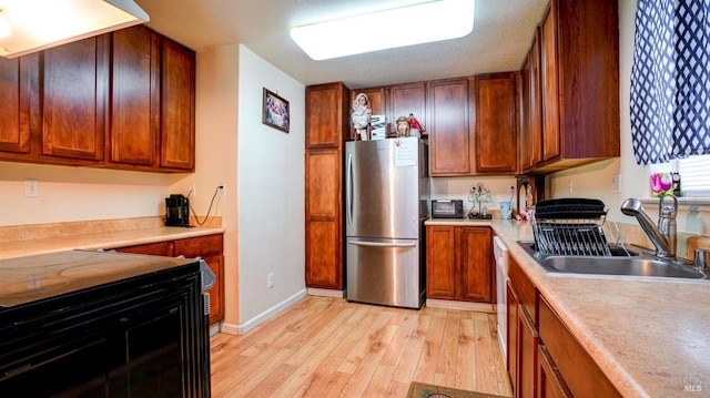 kitchen with brown cabinets, light wood finished floors, light countertops, freestanding refrigerator, and a sink