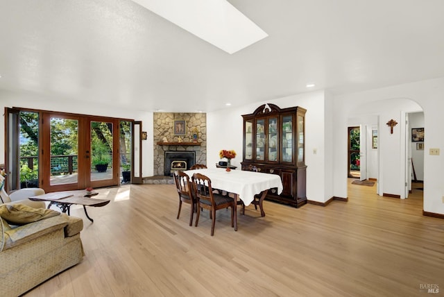 dining space featuring french doors, a stone fireplace, a skylight, and light wood-type flooring