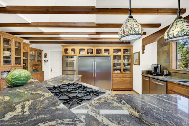 kitchen with beamed ceiling, appliances with stainless steel finishes, decorative light fixtures, and dark stone counters