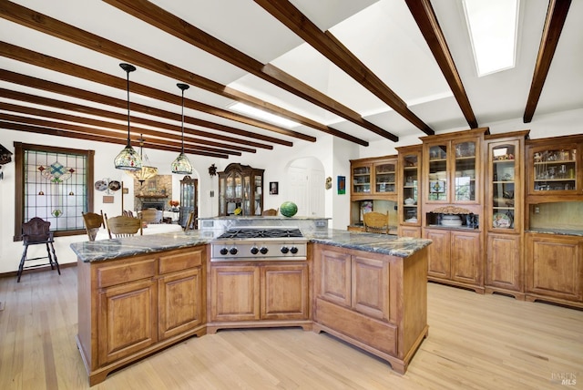 kitchen with decorative light fixtures, stainless steel gas stovetop, dark stone countertops, beam ceiling, and light hardwood / wood-style flooring