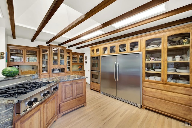 kitchen featuring stainless steel appliances, dark stone countertops, light wood-type flooring, and beamed ceiling