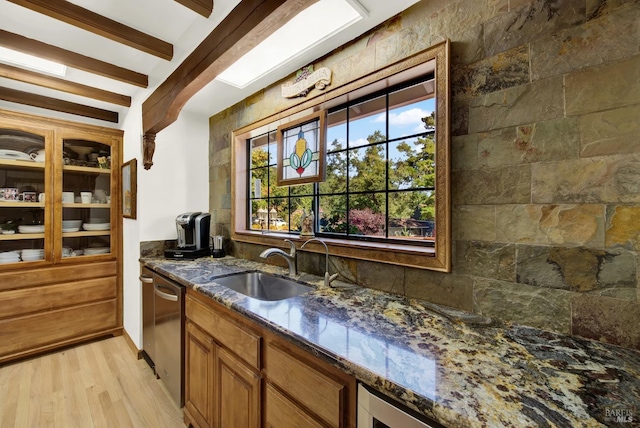 bar featuring sink, light hardwood / wood-style flooring, dark stone countertops, beam ceiling, and stainless steel dishwasher