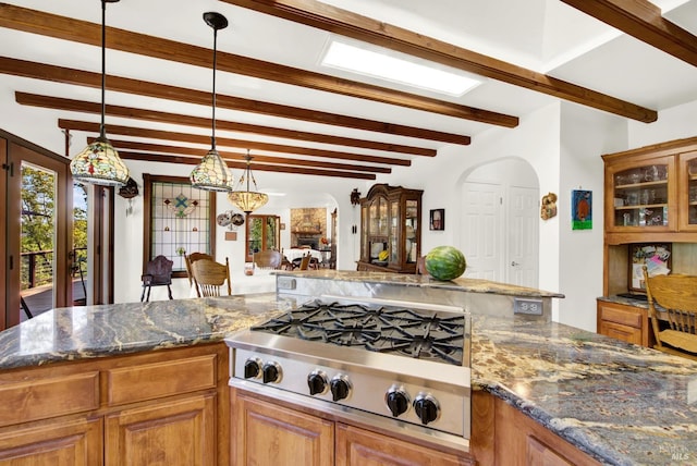 kitchen with beamed ceiling, stainless steel gas stovetop, decorative light fixtures, and dark stone countertops