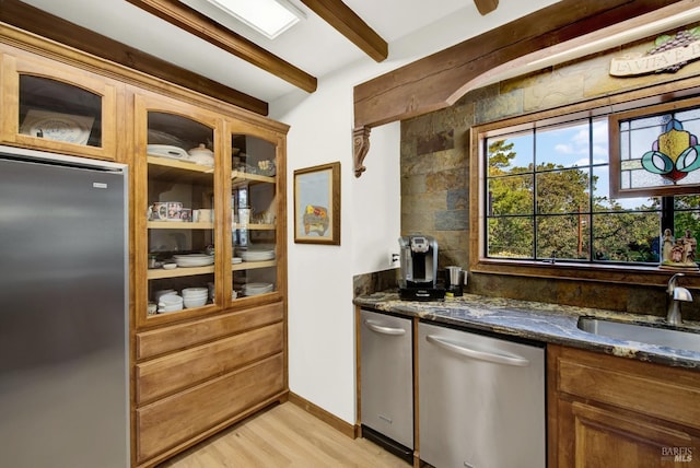 kitchen with sink, light hardwood / wood-style flooring, dark stone countertops, beam ceiling, and stainless steel appliances