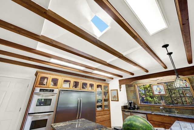 kitchen with dark stone countertops, hanging light fixtures, beam ceiling, and stainless steel appliances