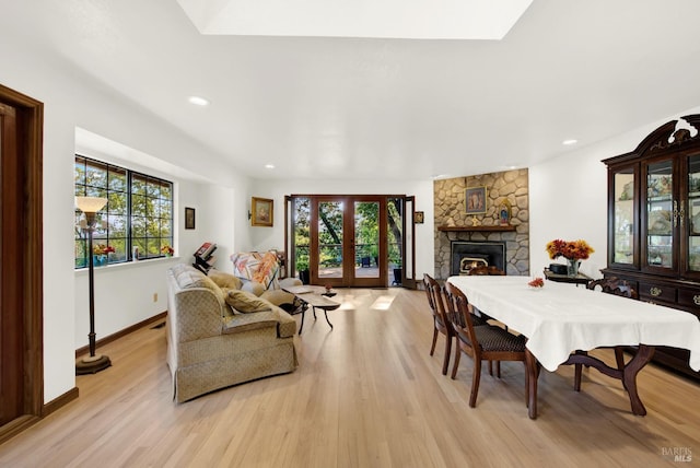 dining room featuring french doors, a stone fireplace, and light wood-type flooring