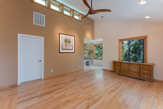 empty room featuring high vaulted ceiling, light wood finished floors, visible vents, and a healthy amount of sunlight