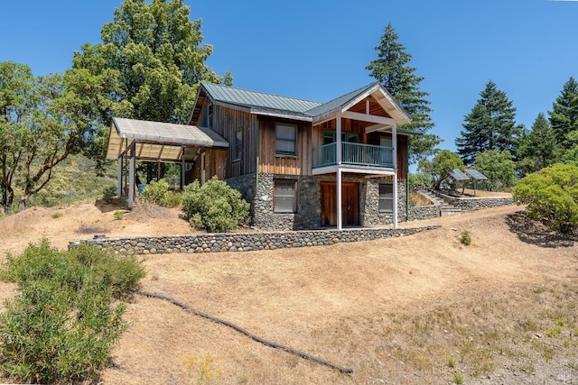 view of front facade featuring metal roof, stone siding, a standing seam roof, and a balcony