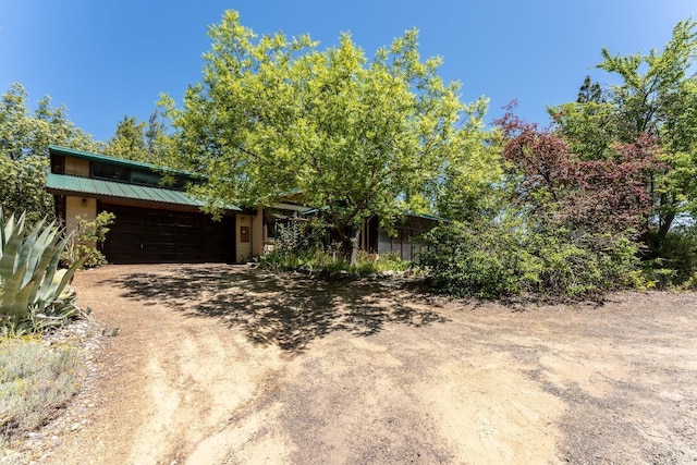 view of front of home featuring an attached garage, metal roof, and dirt driveway