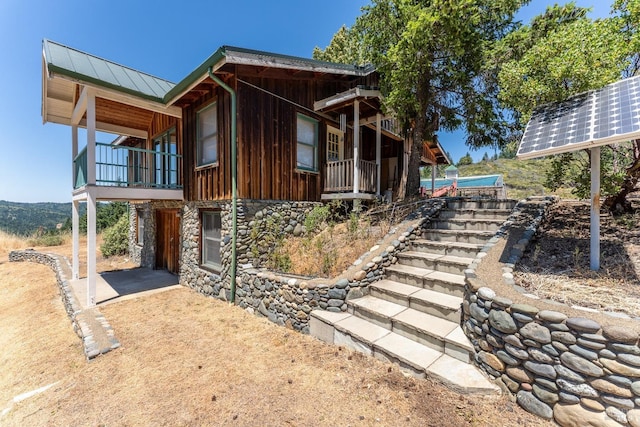 view of property exterior featuring stone siding, ground mounted solar panels, metal roof, a standing seam roof, and board and batten siding