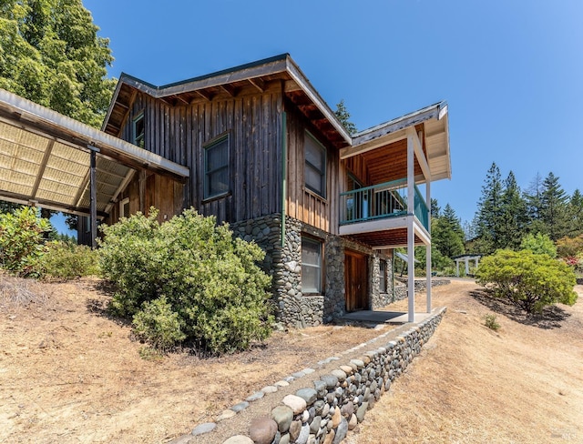 view of home's exterior with a balcony, stone siding, and board and batten siding