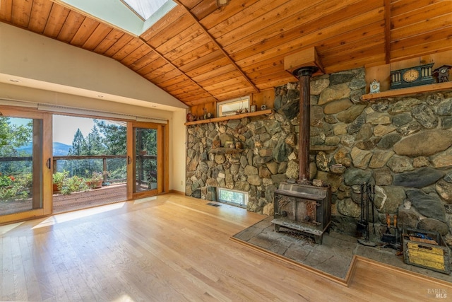 unfurnished living room with lofted ceiling with skylight, wooden ceiling, a wood stove, and light wood-style floors