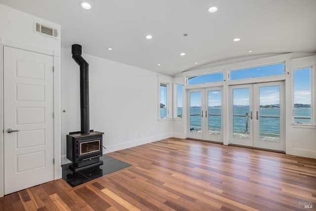 living room with french doors, a water view, a wood stove, and lofted ceiling