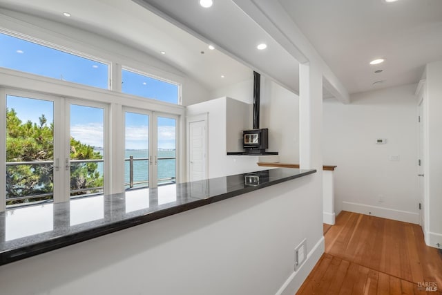 kitchen with a wood stove, high vaulted ceiling, dark stone countertops, hardwood / wood-style floors, and a water view