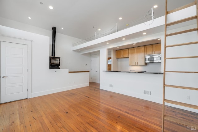 unfurnished living room with hardwood / wood-style floors, a wood stove, and a high ceiling