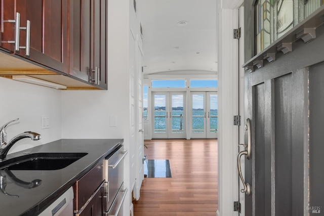 kitchen with dishwasher, french doors, sink, dark hardwood / wood-style flooring, and a water view