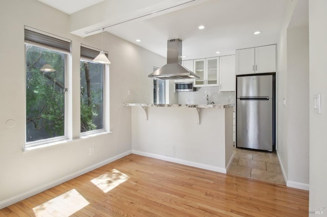 kitchen with island exhaust hood, glass insert cabinets, white cabinetry, a breakfast bar area, and stainless steel appliances