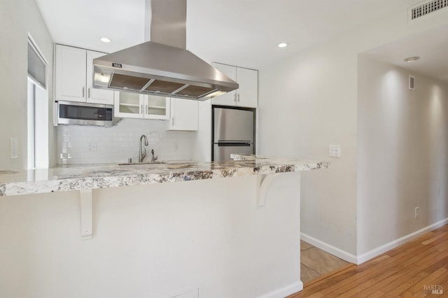 kitchen featuring tasteful backsplash, a kitchen bar, island exhaust hood, stainless steel appliances, and white cabinets