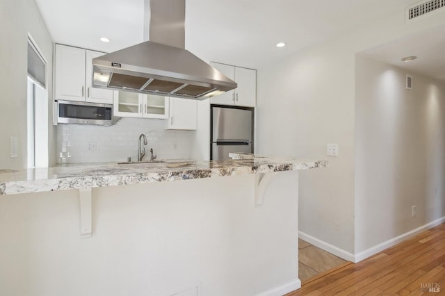 kitchen with white cabinetry, visible vents, appliances with stainless steel finishes, island range hood, and a breakfast bar area