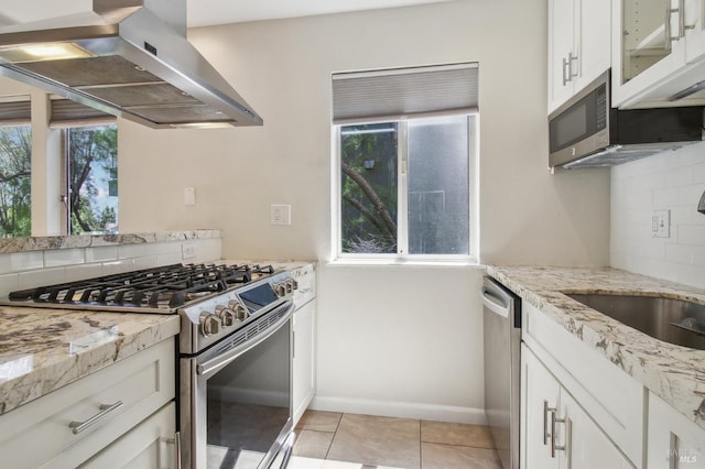 kitchen featuring stainless steel appliances, range hood, decorative backsplash, and a healthy amount of sunlight