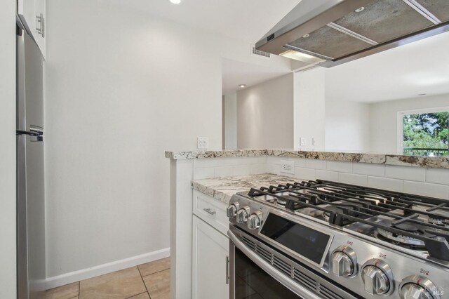 kitchen with light tile patterned floors, wall chimney range hood, white cabinetry, light stone counters, and stainless steel appliances