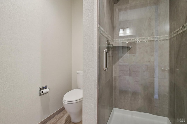 bathroom with a textured wall, a stall shower, toilet, and wood finished floors