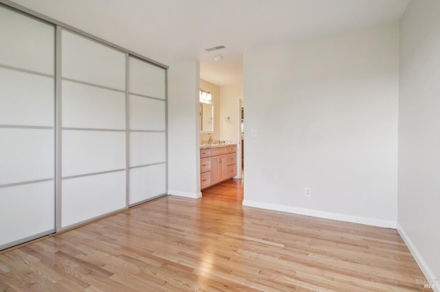 unfurnished bedroom featuring ensuite bathroom, light wood-type flooring, sink, and a closet