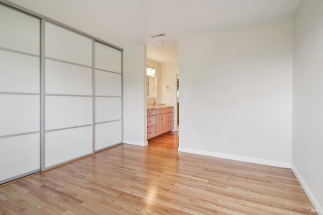 unfurnished bedroom with baseboards, connected bathroom, visible vents, light wood finished floors, and a sink
