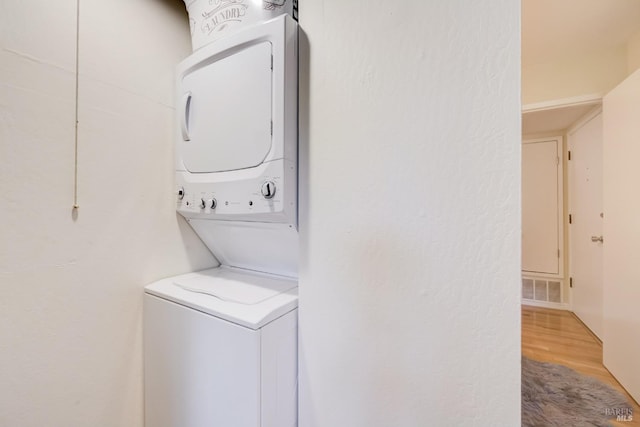 washroom featuring stacked washing maching and dryer, visible vents, laundry area, and wood finished floors
