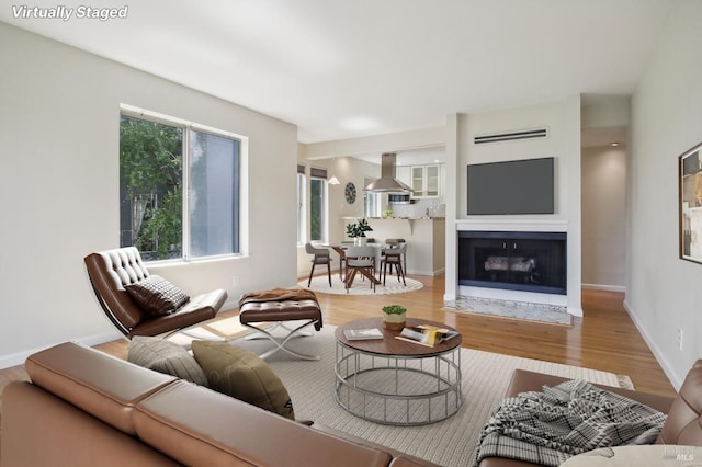 living room with a fireplace with flush hearth, wood finished floors, a wall unit AC, and baseboards