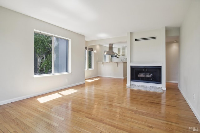 unfurnished living room with a fireplace with flush hearth, light wood-style floors, and baseboards