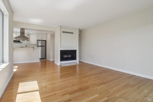 unfurnished living room featuring a fireplace with flush hearth, light wood finished floors, and baseboards