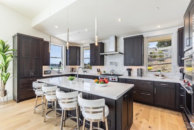 kitchen with light hardwood / wood-style flooring, a wealth of natural light, decorative backsplash, and wall chimney exhaust hood