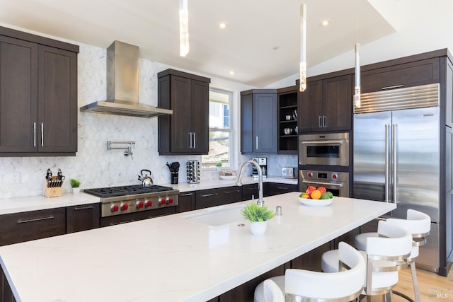 kitchen featuring tasteful backsplash, light hardwood / wood-style floors, appliances with stainless steel finishes, wall chimney exhaust hood, and a kitchen bar