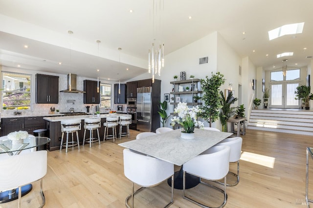 dining space featuring plenty of natural light, high vaulted ceiling, light hardwood / wood-style flooring, and a skylight