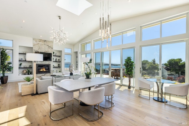 dining area with a fireplace, a chandelier, built in features, a skylight, and light hardwood / wood-style floors