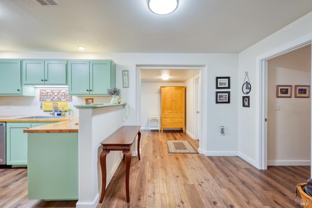 kitchen featuring butcher block countertops, green cabinetry, light hardwood / wood-style floors, and sink