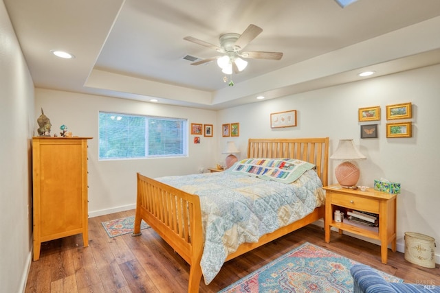 bedroom with hardwood / wood-style floors, a tray ceiling, and ceiling fan