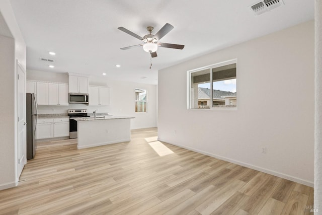 kitchen with light hardwood / wood-style flooring, an island with sink, ceiling fan, stainless steel appliances, and white cabinets