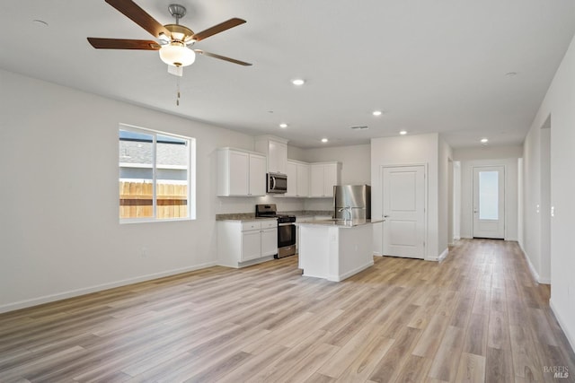 kitchen featuring appliances with stainless steel finishes, a kitchen island with sink, white cabinetry, light stone counters, and light wood-type flooring