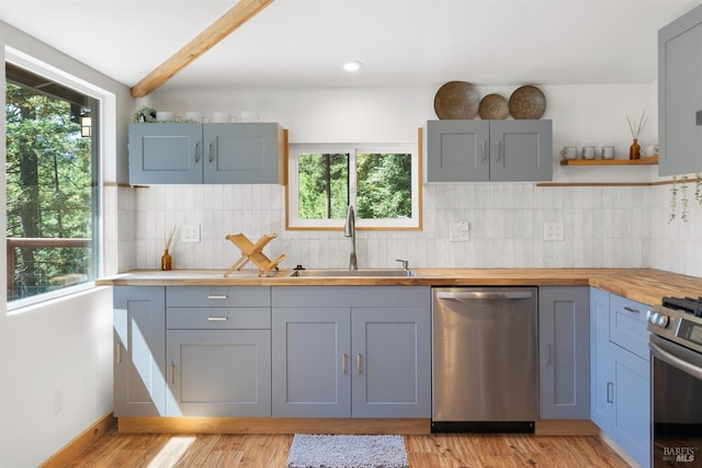 kitchen featuring sink, light hardwood / wood-style flooring, appliances with stainless steel finishes, tasteful backsplash, and beamed ceiling