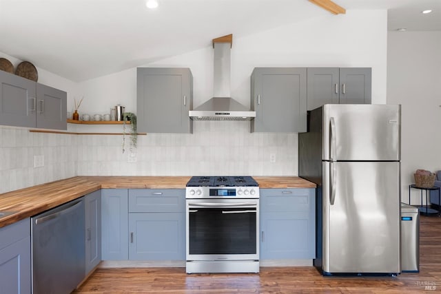 kitchen with wall chimney exhaust hood, wood counters, stainless steel appliances, and vaulted ceiling with beams