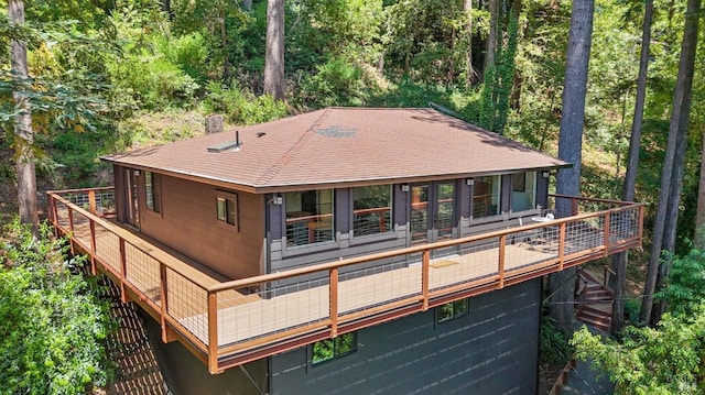 rear view of house featuring a shingled roof and a wooded view