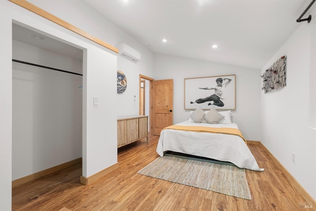 bedroom with a wall mounted air conditioner, vaulted ceiling, and light wood-type flooring