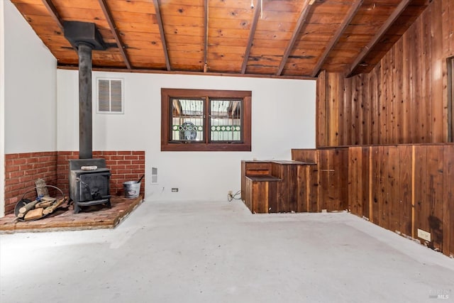 unfurnished living room featuring concrete flooring, wooden walls, lofted ceiling with beams, a wood stove, and wooden ceiling