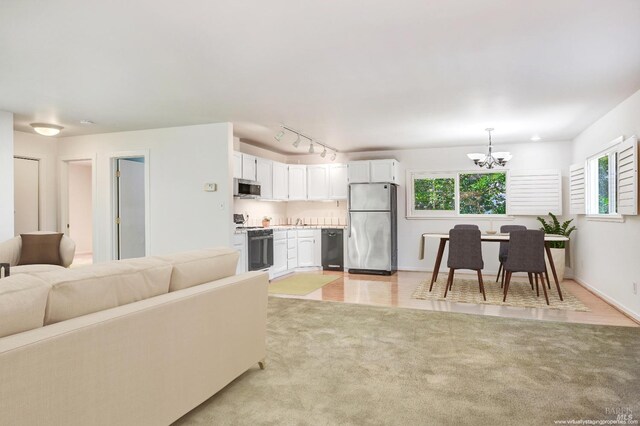 living room featuring a chandelier, rail lighting, a wealth of natural light, and light colored carpet