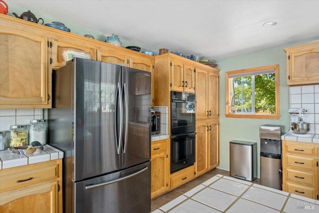 kitchen with stainless steel refrigerator, light tile patterned floors, decorative backsplash, tile countertops, and double oven