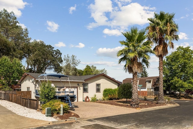 ranch-style home featuring driveway, an attached garage, fence, and stucco siding